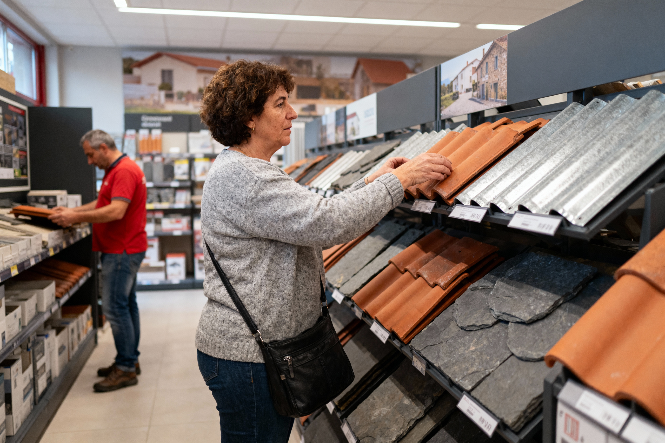 pexels-michal-pech-213601-757318 (1) Une femme examine des tuiles dans un magasin de bricolage, tandis qu'un homme en arrière-plan consulte des produits.