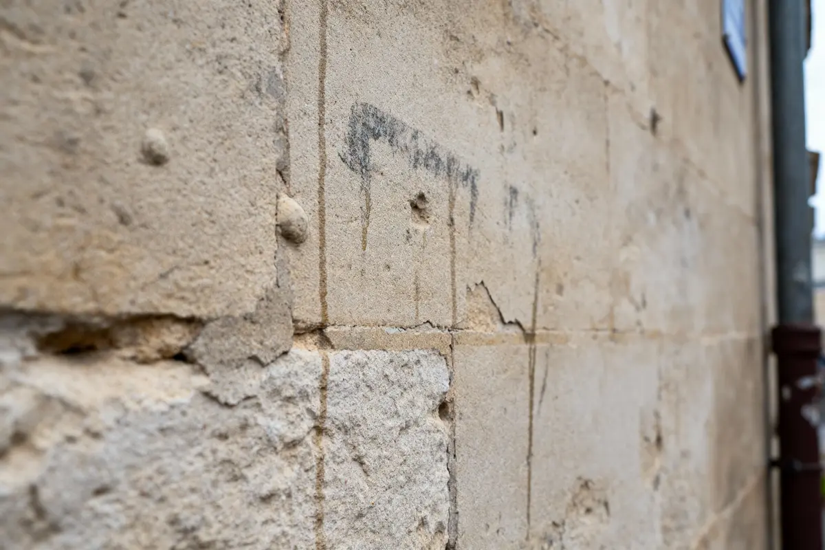 pexels-michal-pech-213601-757318 (1) Gros plan mur en pierre beige avec fissures et taches noires, aspect ancien et usé.