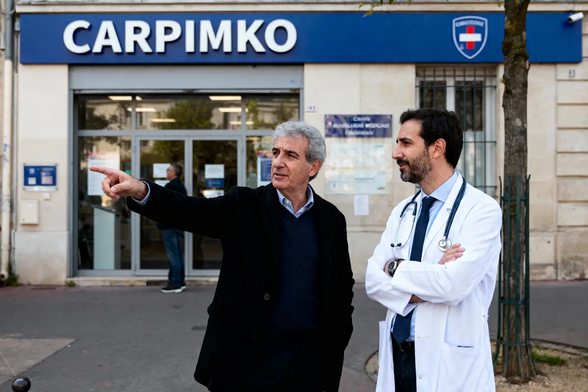 pexels-michal-pech-213601-757318 (1) Deux hommes discutent devant un bâtiment CARPIMKO, l'un en costume, l'autre en blouse médicale avec stéthoscope.