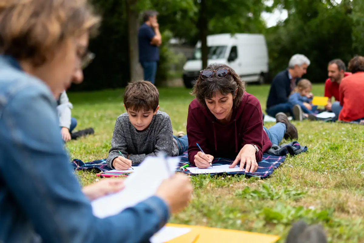 pexels-michal-pech-213601-757318 (1) Personnes écrivant allongées sur une couverture dans un parc, ambiance détendue avec arbres en arrière-plan.