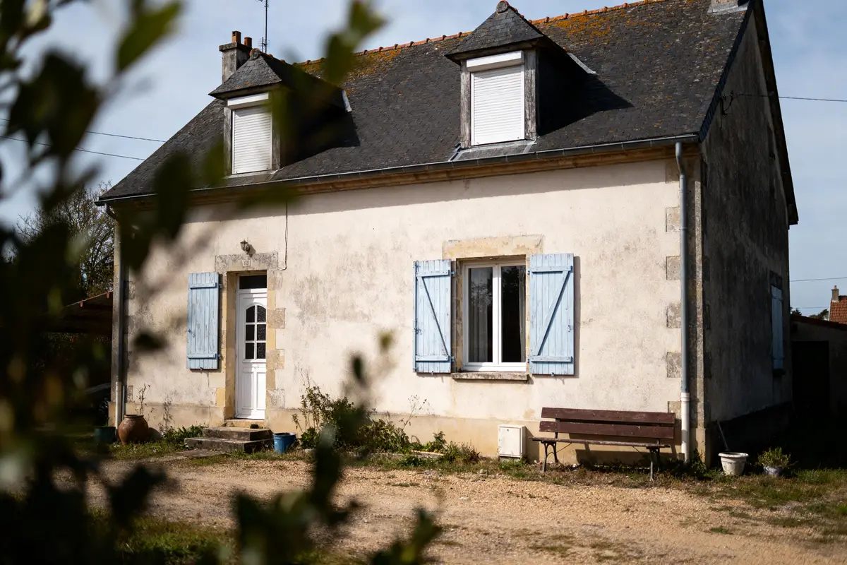 pexels-michal-pech-213601-757318 (1) Maison ancienne avec toit ardoise, volets bleus, et végétation au premier plan par journée ensoleillée.